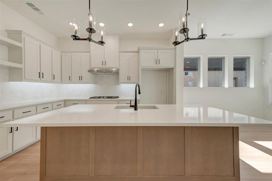 Modern kitchen featuring a large central island with a light-toned wood-finish base and expansive light-colored countertop Modern kitchen featuring a large central island with a light-toned wood-finish base and expansive light-colored countertop