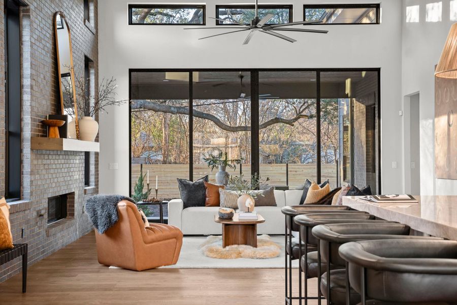 Living area with healthy amount of natural light, wood finished floors, a brick fireplace, and a towering ceiling