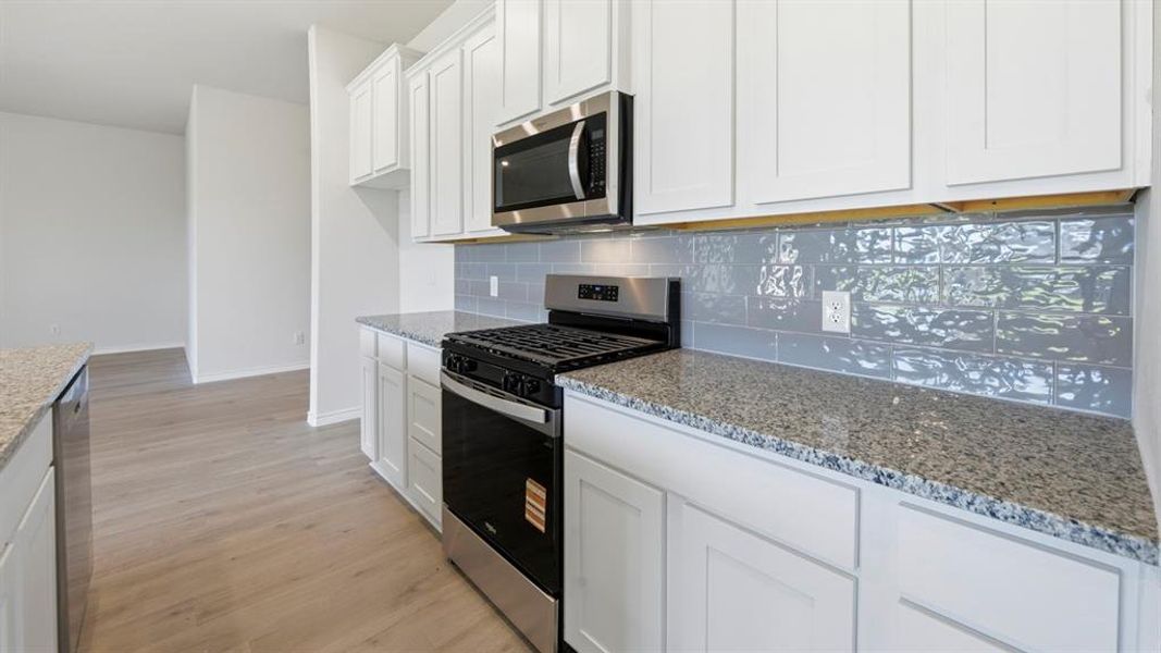 Kitchen featuring appliances with stainless steel finishes, white cabinets, light wood finished floors, and light stone counters