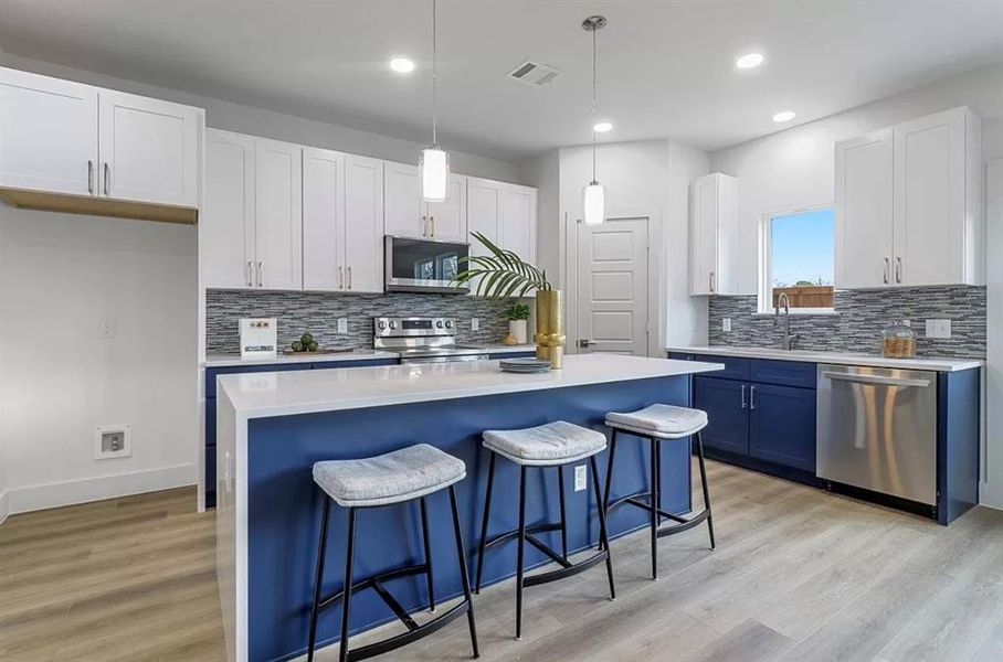 Kitchen with light hardwood / wood-style flooring, backsplash, a kitchen island, stainless steel appliances, and hanging light fixtures