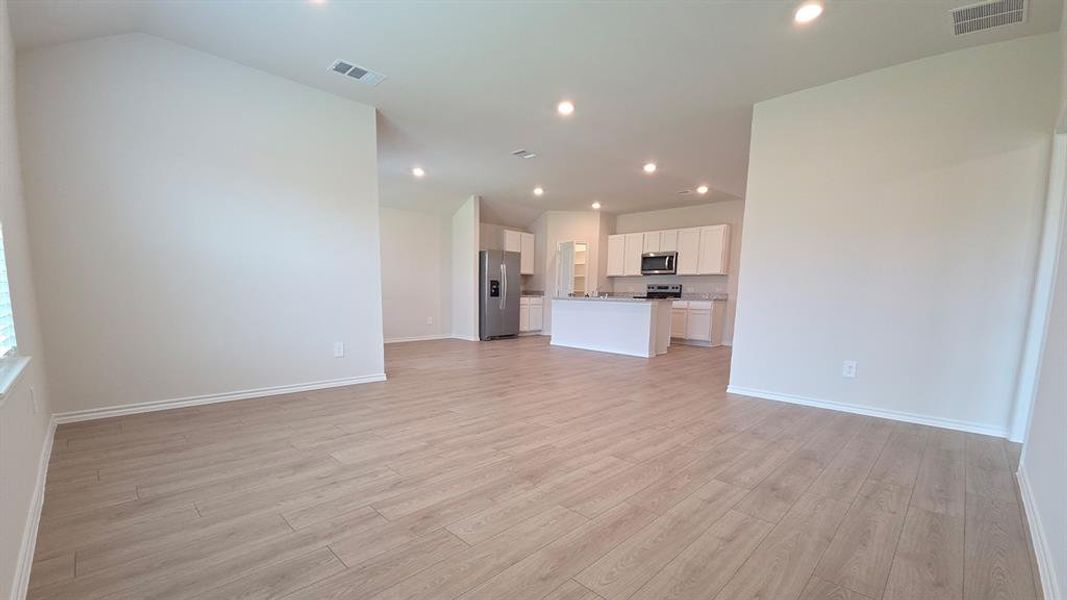 Open-concept living space featuring wood-finish flooring, recessed lighting, vaulted ceilings, and a kitchen with an island and stainless steel appliances