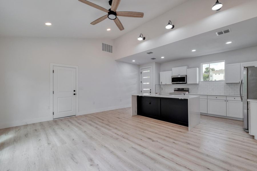 A contemporary open-concept space features light wood flooring, an airy ceiling with a ceiling fan, and a sleek kitchen island. A contemporary open-concept space features light wood flooring, an airy ceiling with a ceiling fan, and a sleek kitchen island.