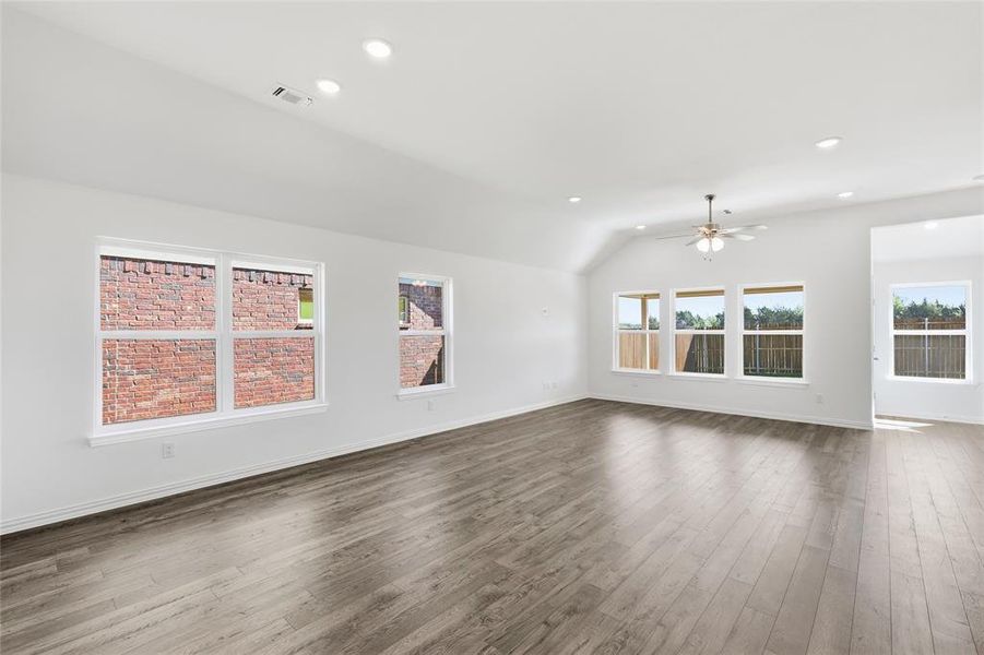Open-concept living area featuring wood-finish flooring, white walls, and a vaulted ceiling