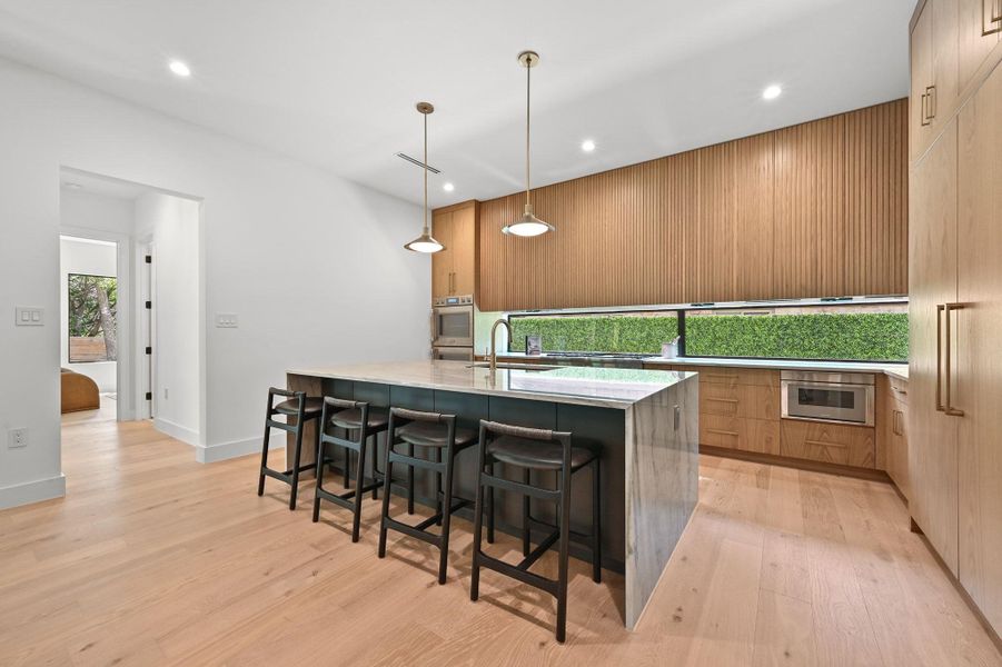 Kitchen featuring light stone counters, modern cabinets, a breakfast bar area, decorative light fixtures, and light wood-style flooring