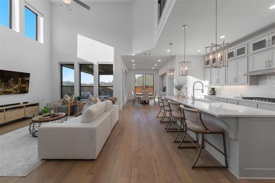 Living area with visible vents, a towering ceiling, wood finished floors, baseboards, and ceiling fan with notable chandelier