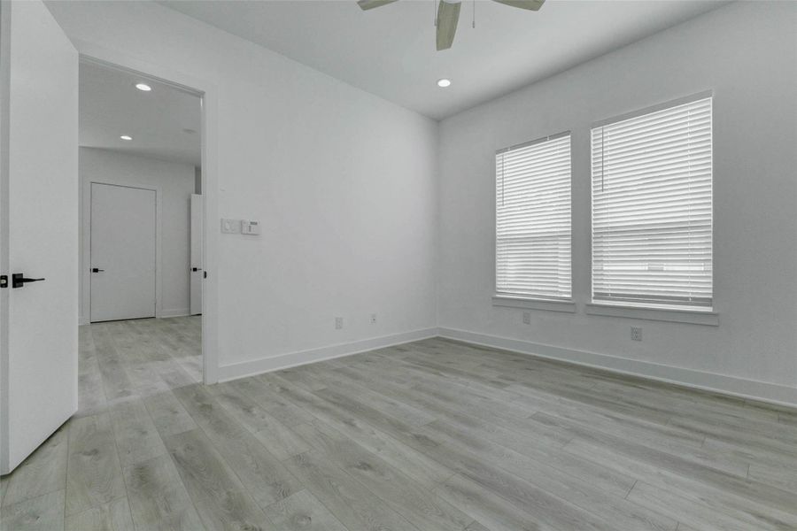 An additional angle emphasizes the bedroom’s open floor area and flexible furniture placement. The visible glass-enclosed shower and coordinated finishes provide a glimpse of the polished primary bathroom beyond.