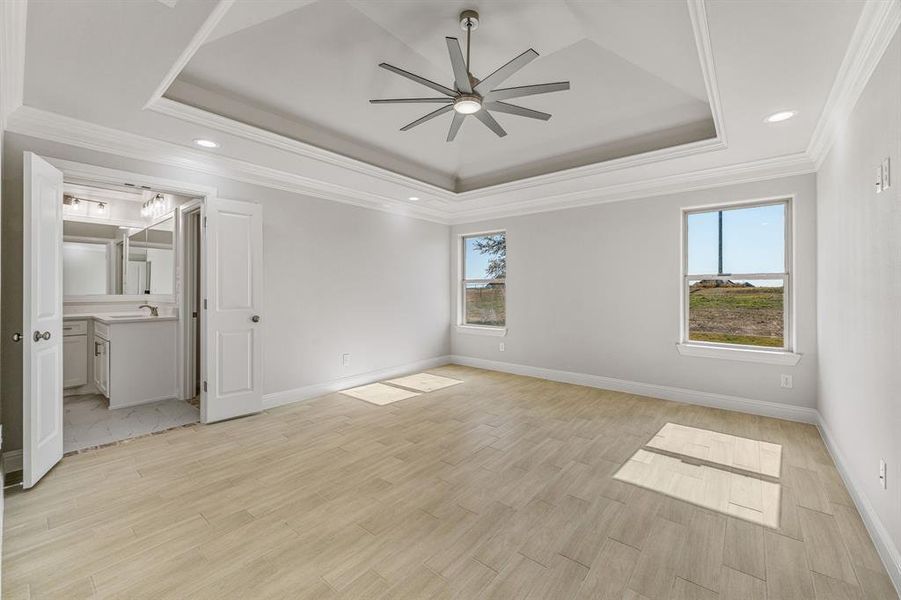 Unfurnished bedroom with ornamental molding, light wood-type flooring, a tray ceiling, ceiling fan, and recessed lighting