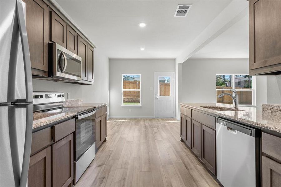 Kitchen with visible vents, appliances with stainless steel finishes, light stone counters, light wood-style floors, and a sink