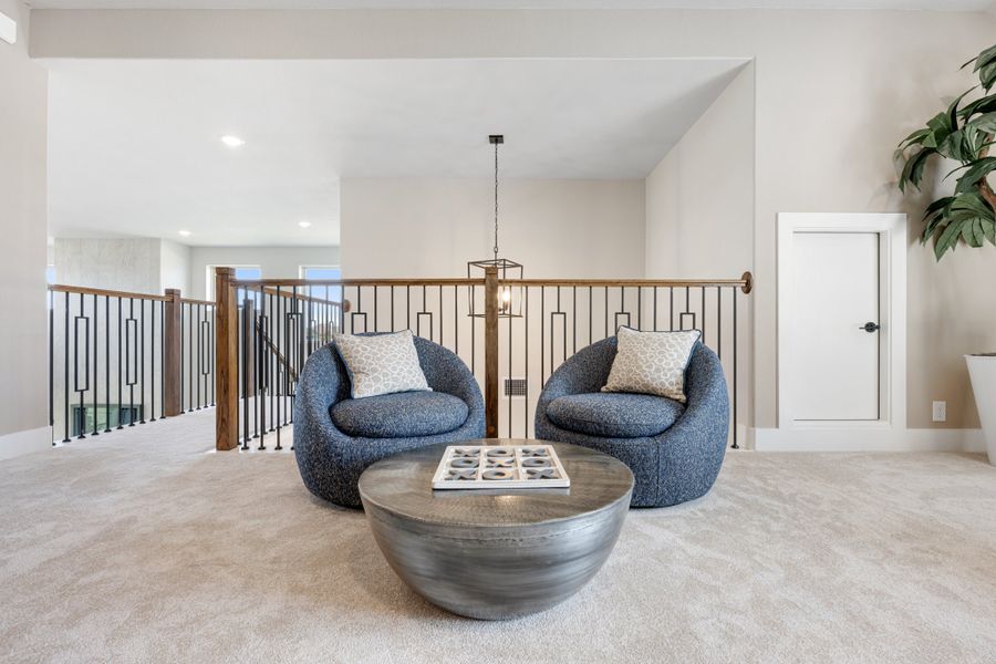 Upstairs loft sitting area with two blue accent chairs, round metal coffee table, and decorative iron stair railing