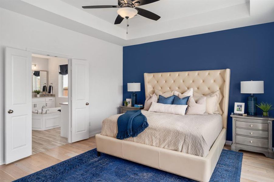 Bedroom featuring light hardwood / wood-style flooring, ensuite bathroom, a raised ceiling, and ceiling fan