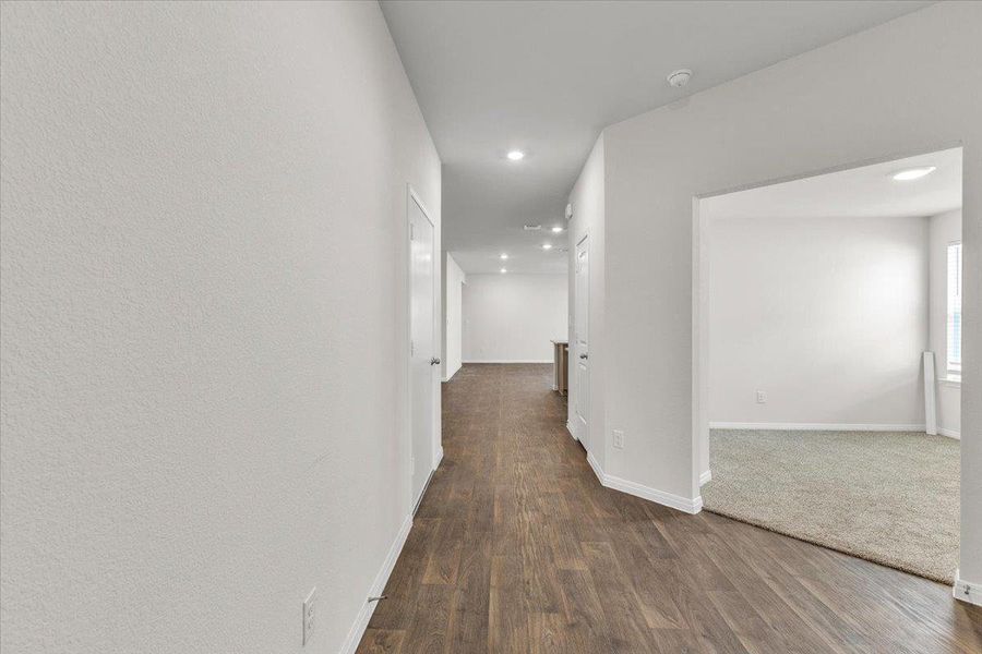 The property features a hallway with wood-look flooring and recessed lighting, leading to an open doorway that reveals a carpeted room with white walls