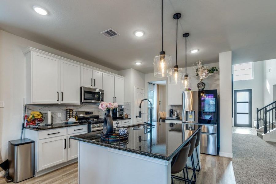 This modern kitchen features sleek white cabinetry, stainless steel appliances, and a large island with pendant lighting. The open layout flows into a well-lit dining area, creating a welcoming space for cooking and entertaining.