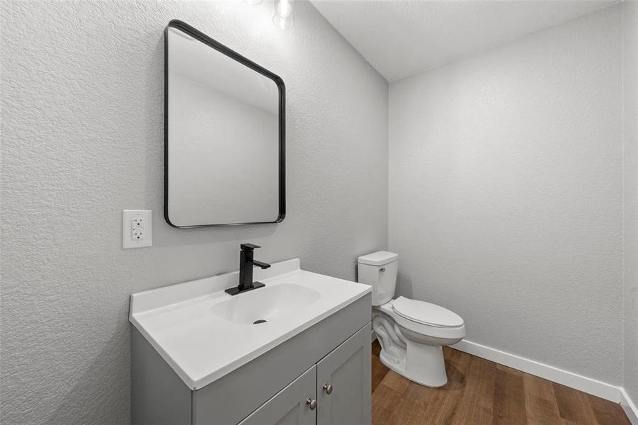 Half bath featuring wood finished floors, vanity, and a textured wall Half bath featuring wood finished floors, vanity, and a textured wall
