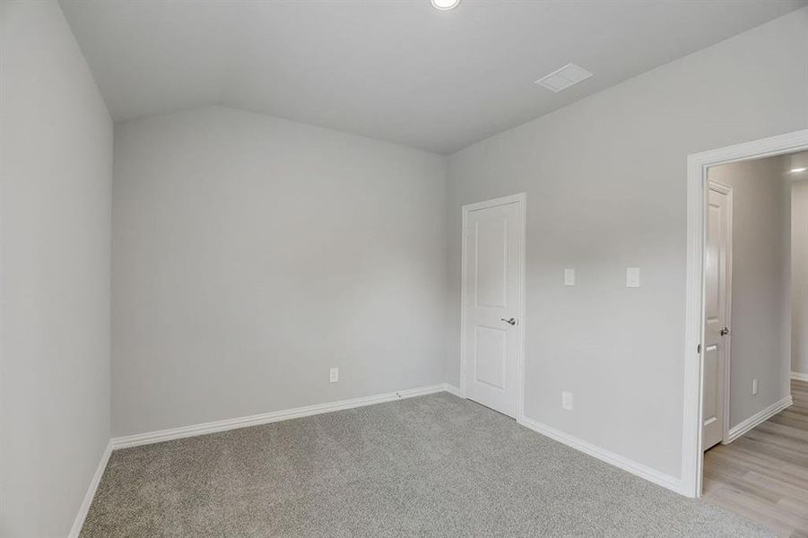 Unfurnished room featuring light carpet and vaulted ceiling