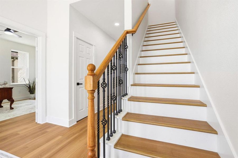 Staircase featuring wood-finish treads, white risers, and a wrought iron balustrade with a wood-finish handrail Staircase featuring wood-finish treads, white risers, and a wrought iron balustrade with a wood-finish handrail