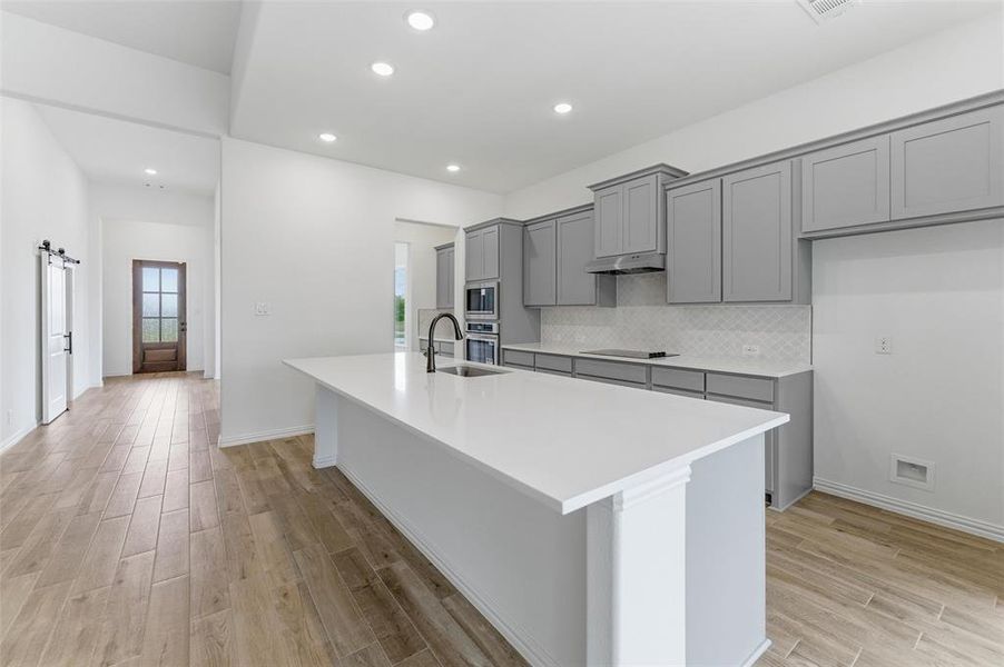 The kitchen features a large island with a white countertop and a sink with a dark faucet, grey cabinetry, and a white tile backsplash