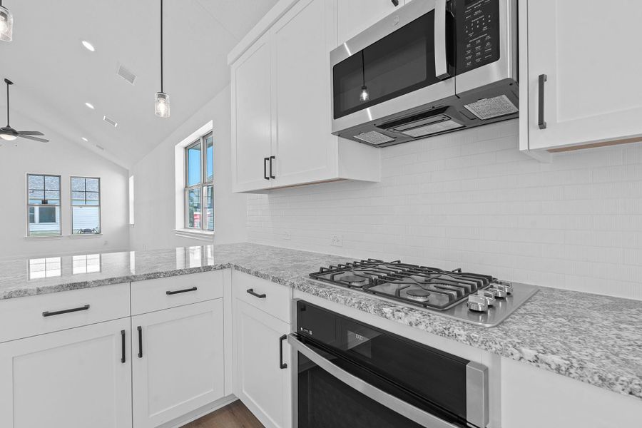 Kitchen featuring white cabinetry, vaulted ceiling, stainless steel appliances, light stone countertops, and tasteful backsplash Kitchen featuring white cabinetry, vaulted ceiling, stainless steel appliances, light stone countertops, and tasteful backsplash