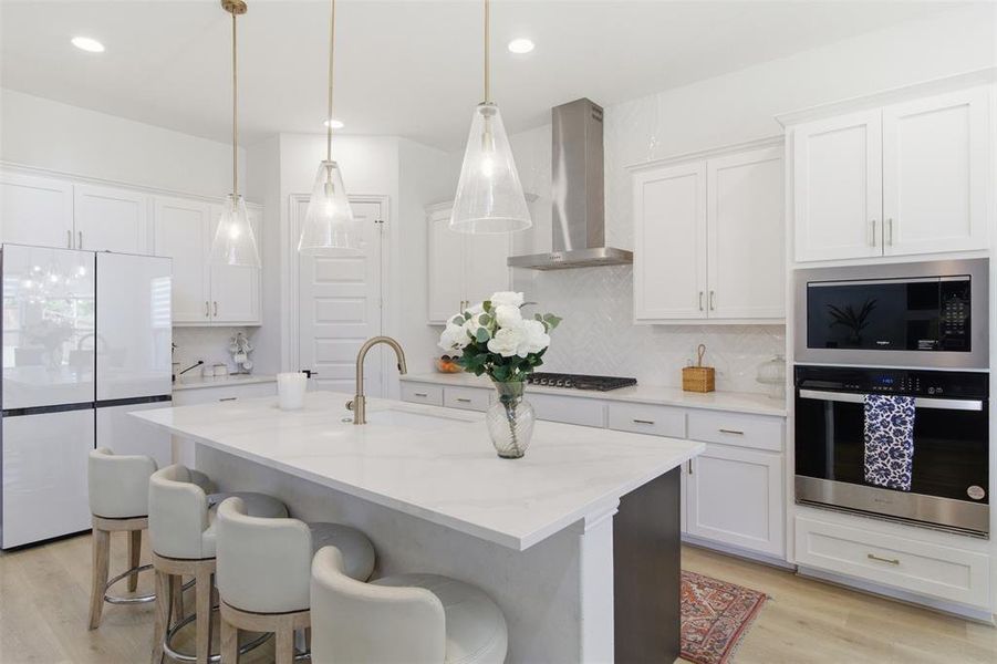 Gourmet kitchen featuring a central island with countertop seating, stainless steel appliances, a range hood, and pendant lighting