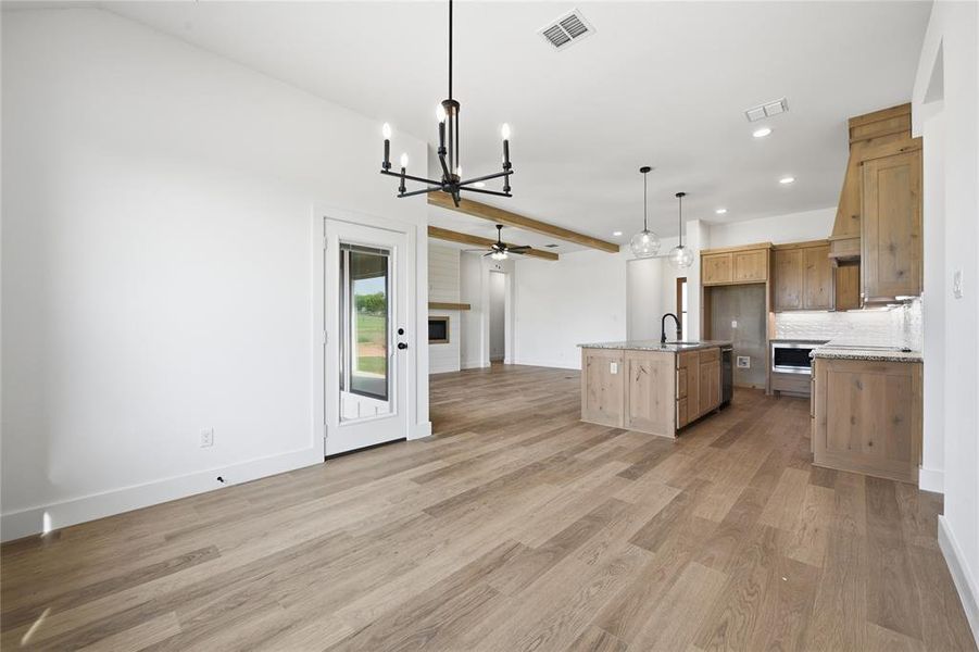 Kitchen with suspended lighting, open floor plan, a center island with sink, a ceiling fan, and light wood-type flooring Kitchen with suspended lighting, open floor plan, a center island with sink, a ceiling fan, and light wood-type flooring