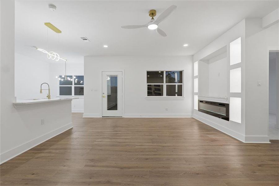 Open-concept living area featuring wood-finish flooring, a built-in media center with an electric fireplace, a contemporary ceiling fan, and recessed lighting