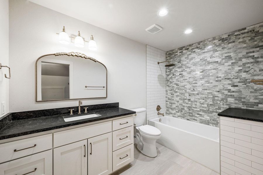Refined full bath featuring black stone counters, white cabinetry, and a custom mirror accented by soft overhead lighting. Refined full bath featuring black stone counters, white cabinetry, and a custom mirror accented by soft overhead lighting.