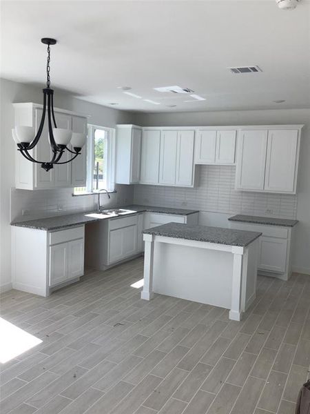 Kitchen featuring an inviting chandelier, a center island, sink, and white cabinets