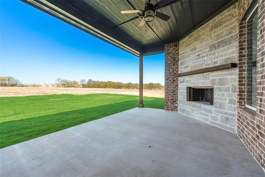 Expansive covered patio featuring a stone fireplace with a wood mantel, a ceiling fan, and brick detailing