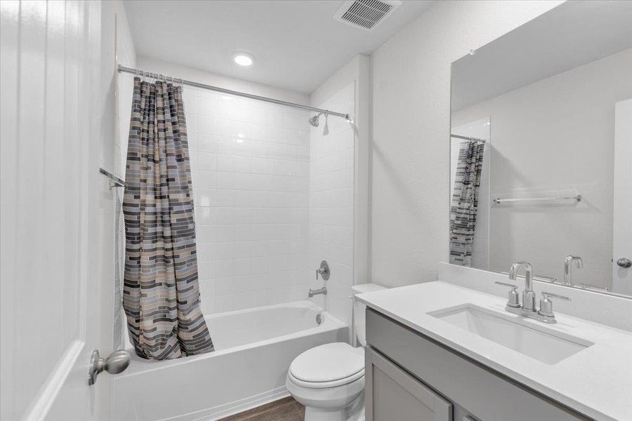 The bathroom features a white bathtub with a tiled surround, a vanity with a white countertop and integrated sink, and a large mirror