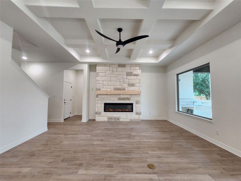 Spacious interior featuring wood-finish flooring, a coffered ceiling with recessed lighting and a ceiling fan, and a stone-clad fireplace with a wood mantel