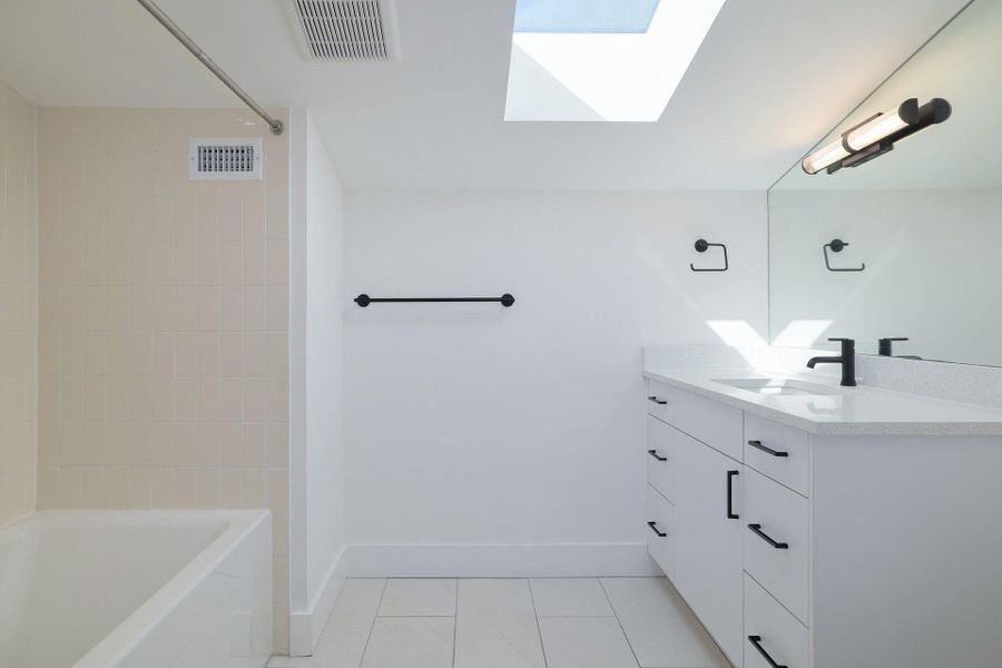 Bathroom with a skylight, vanity, shower / tub combination, and light tile patterned floors