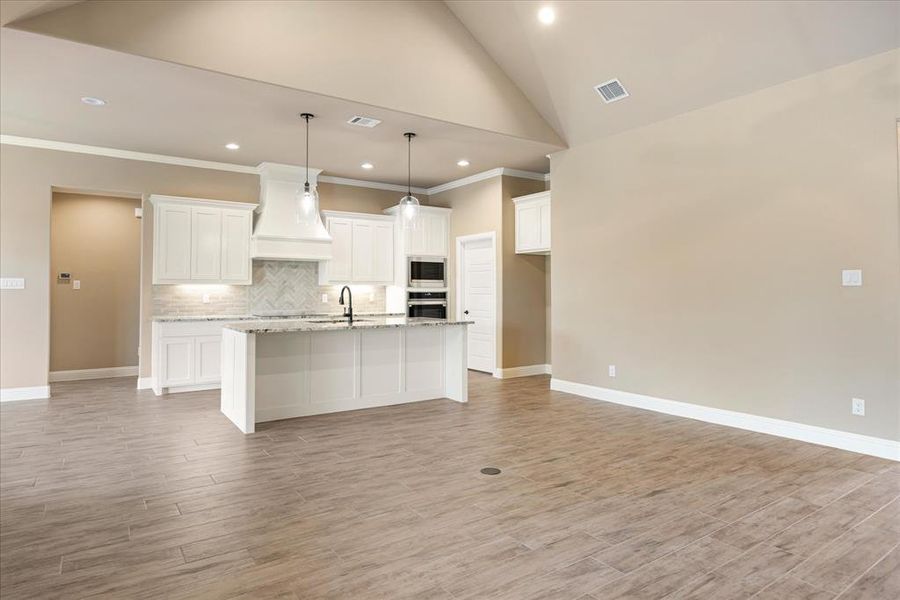 Kitchen featuring a kitchen island with sink, hanging light fixtures, custom range hood, vaulted ceiling, and white cabinets