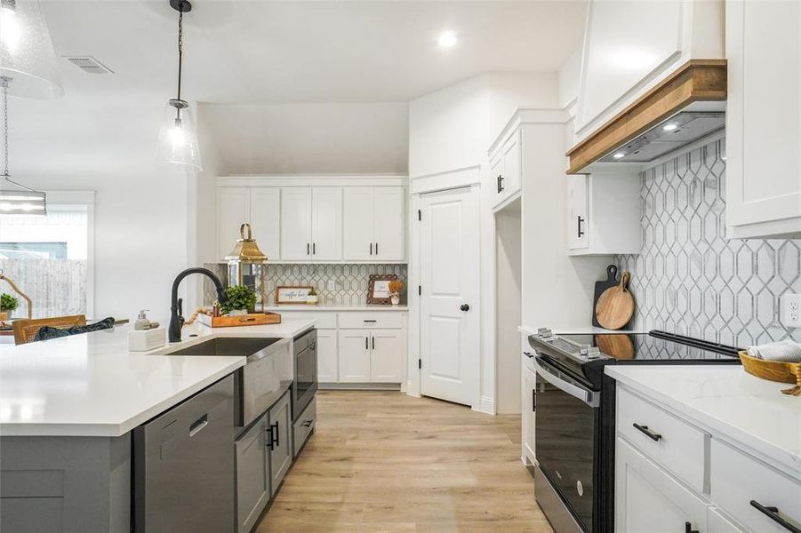 Kitchen featuring backsplash, white cabinets, pendant lighting, and appliances with stainless steel finishes