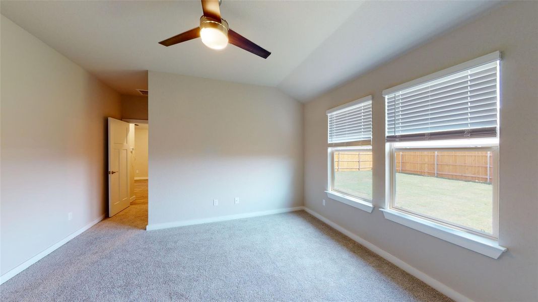 A well-lit bedroom features plush carpeting and backyard views through a pair of windows. A well-lit bedroom features plush carpeting and backyard views through a pair of windows.