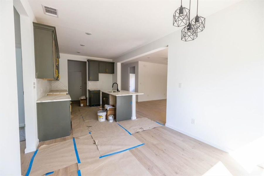 Kitchen featuring hanging light fixtures, backsplash, an island with sink, light wood-type flooring, and sink