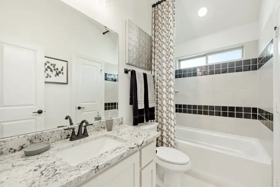 Bathroom with granite countertop, white cabinets, and tiled bathtub with dark accent tiles
