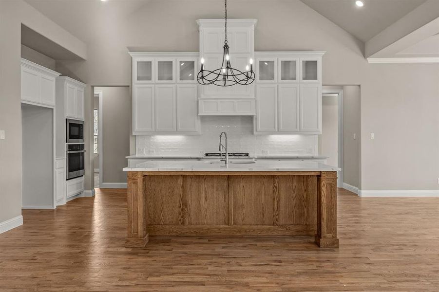 Kitchen with white cabinetry, an island with sink, built in microwave, and stainless steel oven