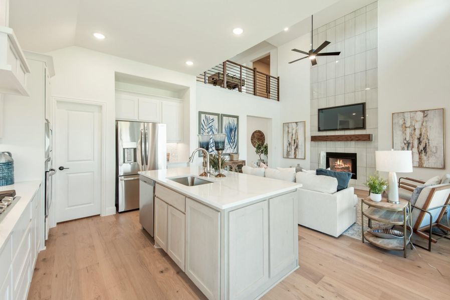 Open-concept kitchen and living area with white island, two-story ceiling, fireplace, and hardwood floors Open-concept kitchen and living area with white island, two-story ceiling, fireplace, and hardwood floors