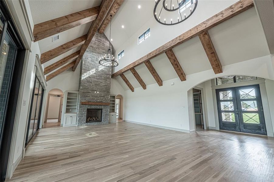 Unfurnished living room featuring arched walkways, high vaulted ceiling, a chandelier, light wood-type flooring, and french doors Unfurnished living room featuring arched walkways, high vaulted ceiling, a chandelier, light wood-type flooring, and french doors