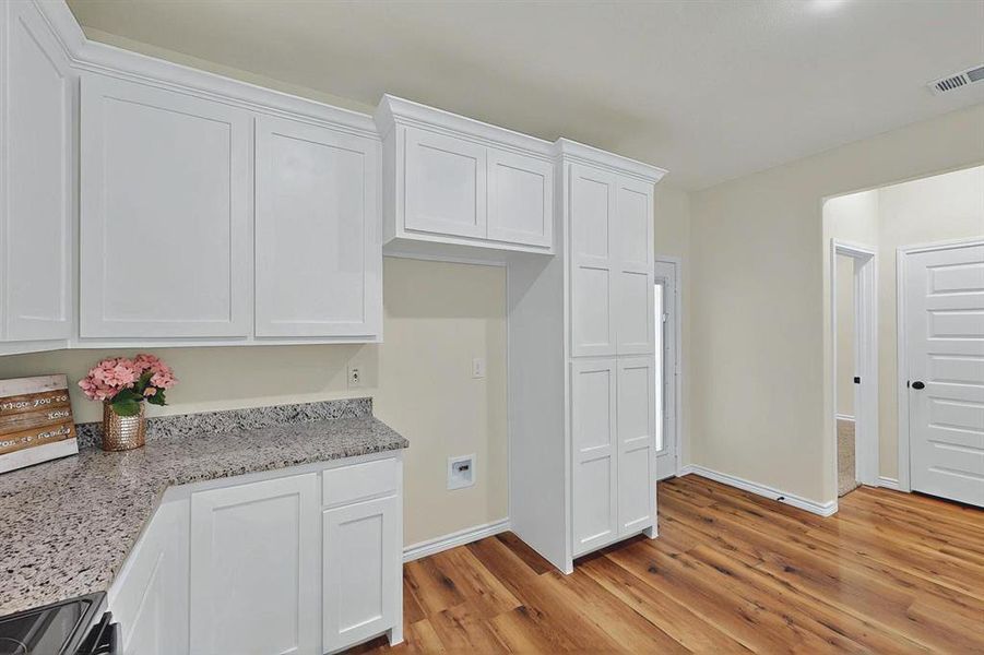 Kitchen with visible vents, stainless steel electric range oven, light wood-type flooring, baseboards, and white cabinetry Kitchen with visible vents, stainless steel electric range oven, light wood-type flooring, baseboards, and white cabinetry