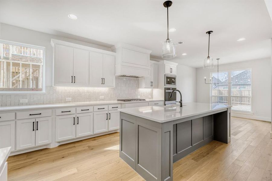 Open-concept kitchen featuring an expansive center island with seating, white shaker cabinetry, a subway tile backsplash, stainless steel appliances, and wood-finish flooring