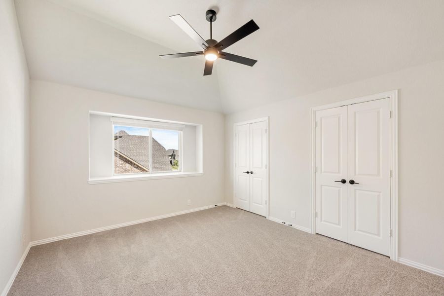 Empty bedroom with vaulted ceiling, black ceiling fan, carpet flooring, and two white double doors Empty bedroom with vaulted ceiling, black ceiling fan, carpet flooring, and two white double doors