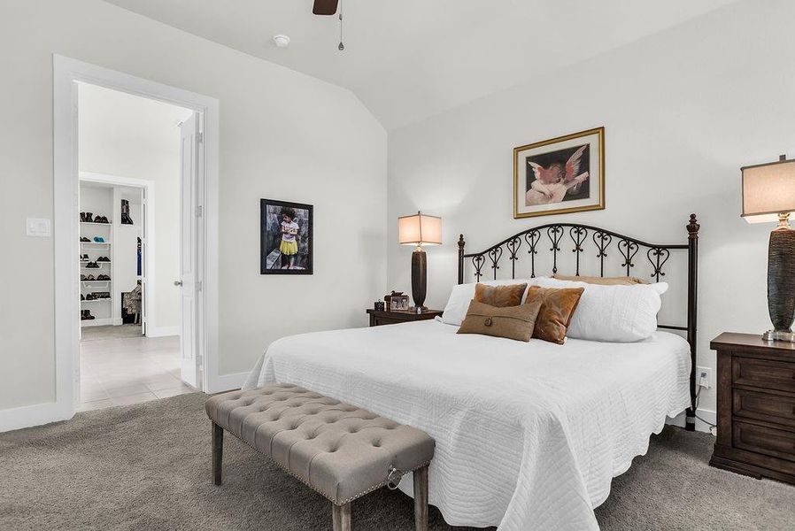 Main bedroom features an ensuite bath, vaulted ceilings, plush carpeting, a ceiling fan with integrated lighting, backyard views, and white walls.