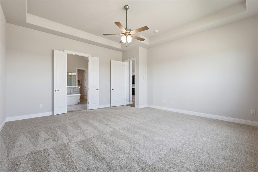 Unfurnished bedroom featuring a tray ceiling, light carpet, a ceiling fan, and connected bathroom Unfurnished bedroom featuring a tray ceiling, light carpet, a ceiling fan, and connected bathroom
