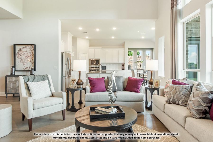 Open-concept living room with neutral sofas, purple accent pillows, and kitchen visible in background