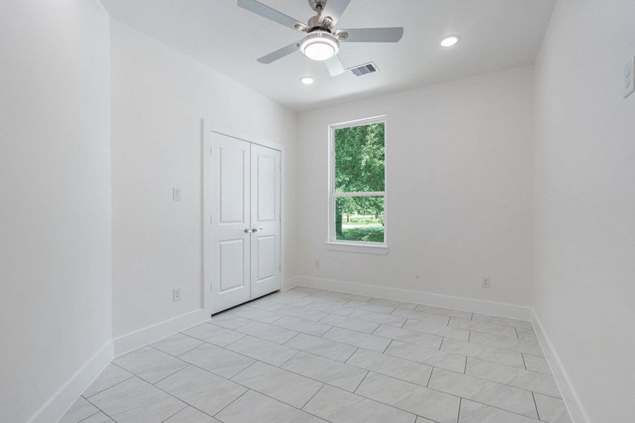 This room features a clean, modern design with white walls and tiled flooring. It includes a ceiling fan, recessed lighting, a window providing natural light, and a closet with double doors. Perfect for a bedroom or home office. This room features a clean, modern design with white walls and tiled flooring. It includes a ceiling fan, recessed lighting, a window providing natural light, and a closet with double doors. Perfect for a bedroom or home office.