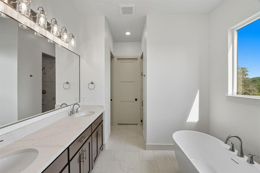 Bathroom featuring a freestanding bath, double vanity, a stall shower, light marble finish flooring, and recessed lighting Bathroom featuring a freestanding bath, double vanity, a stall shower, light marble finish flooring, and recessed lighting