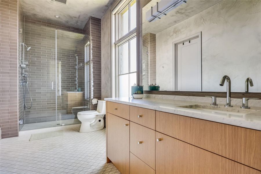 A well-lit bathroom featuring a spacious shower and sleek vanity with ample storage.