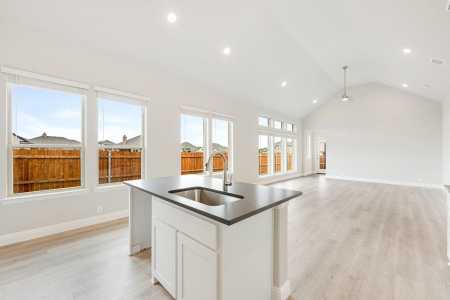 Open-concept kitchen with white island, dark countertop, and sink flowing into living area with vaulted ceiling and light wood floors
