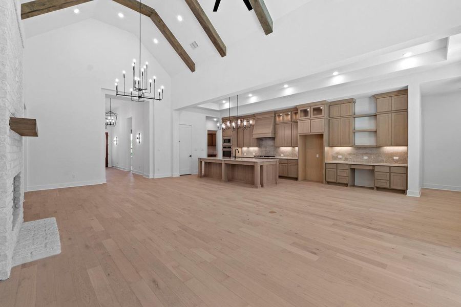 Unfurnished living room with light wood-type flooring, a chandelier, a large fireplace, high vaulted ceiling, and beamed ceiling Unfurnished living room with light wood-type flooring, a chandelier, a large fireplace, high vaulted ceiling, and beamed ceiling