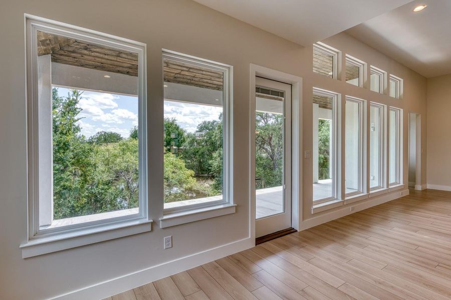 Floor-to-ceiling windows and a glass-paneled door open to a tranquil, tree-filled outdoor space.